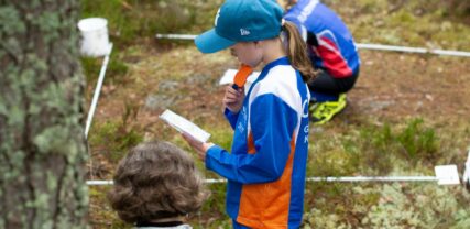 På bilden är tre barn på orienteringskurs i skogen